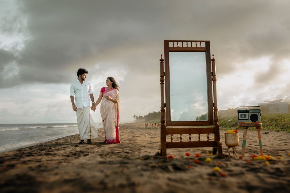 Dramatic beachside photo session with a rustic mirror frame and scattered decorative elements on the sand.