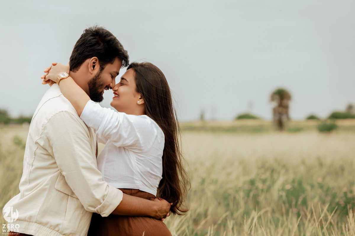 A couple embraces while standing in a golden field during a romantic outdoor photoshoot.