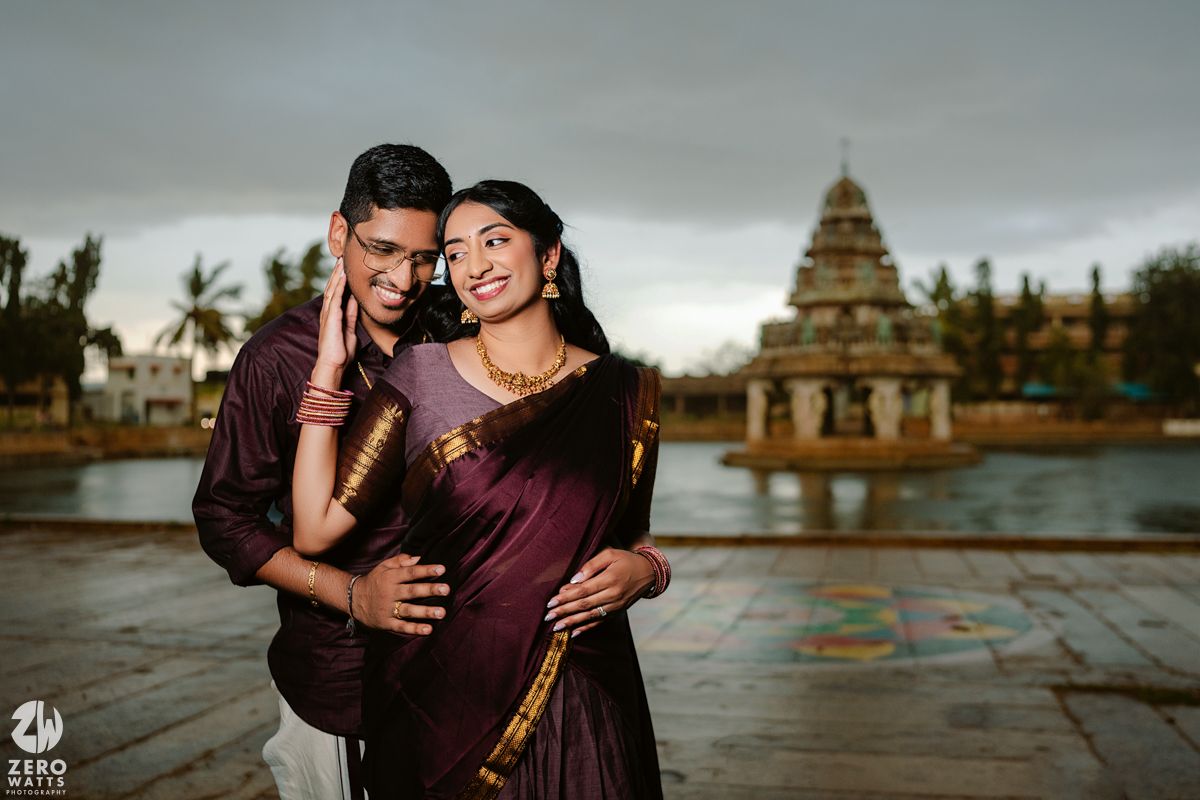 A couple poses together against a scenic temple backdrop with palm trees and water.