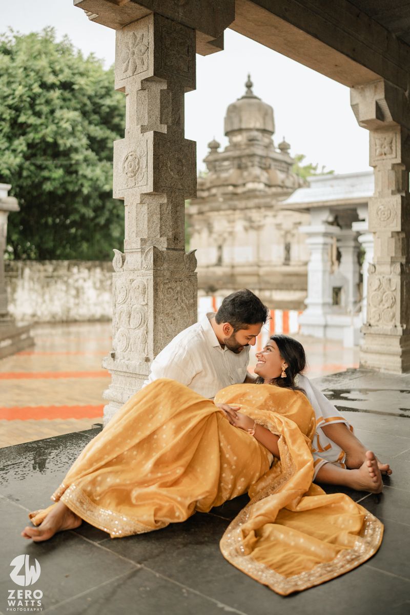 Romantic couple in traditional Indian attire poses gracefully under ornate stone pillars during a photoshoot session.