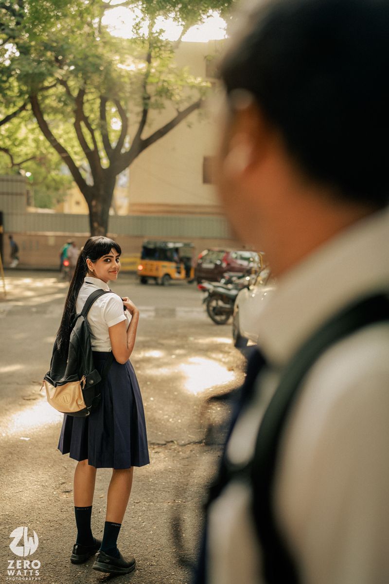 Students in school uniforms walking outdoors on a sunny day with trees in the background.