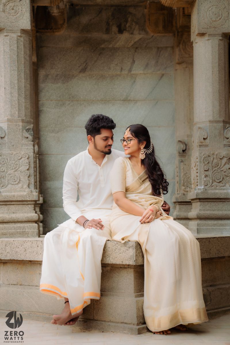 Couple in matching white outfits sit together on a stone ledge at a traditional temple.