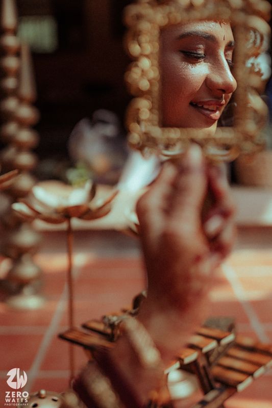 Close-up of a smiling Indian bride reflected in an ornate mirror during a traditional wedding ceremony.