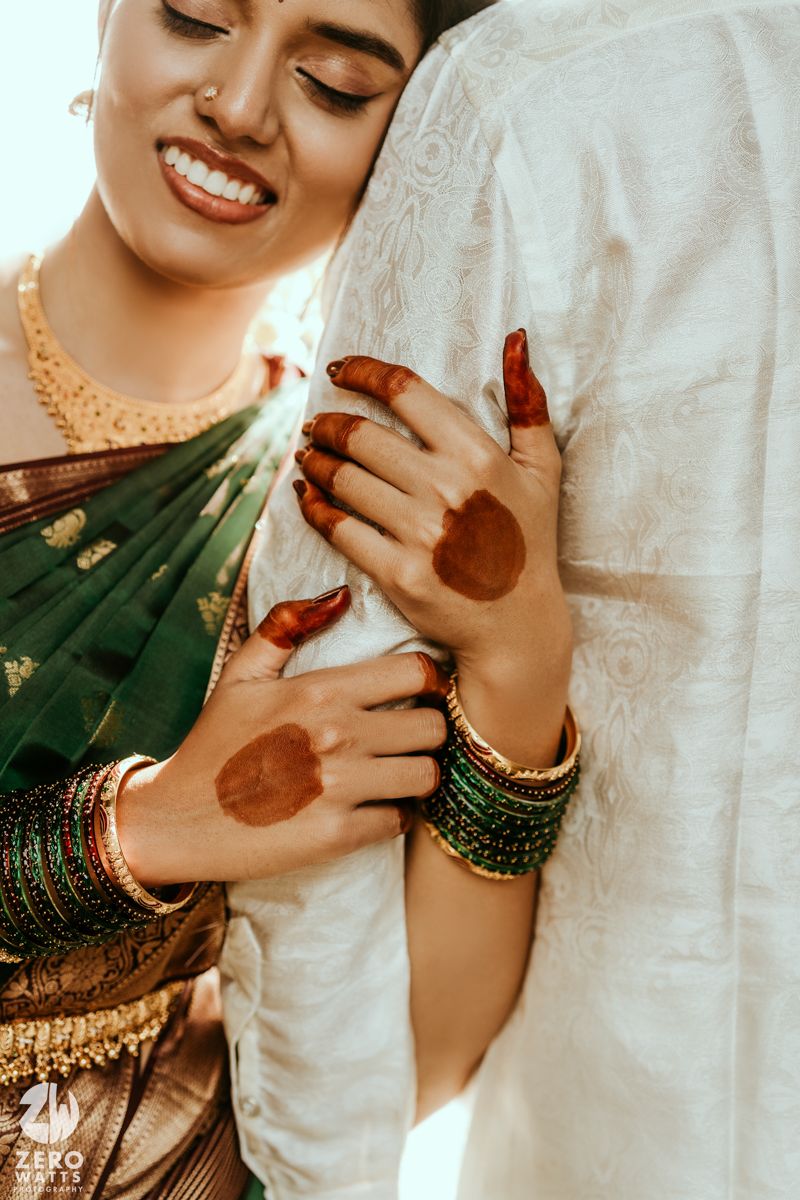 Indian bride in green saree with henna hands and gold bangles embracing groom in white kurta.