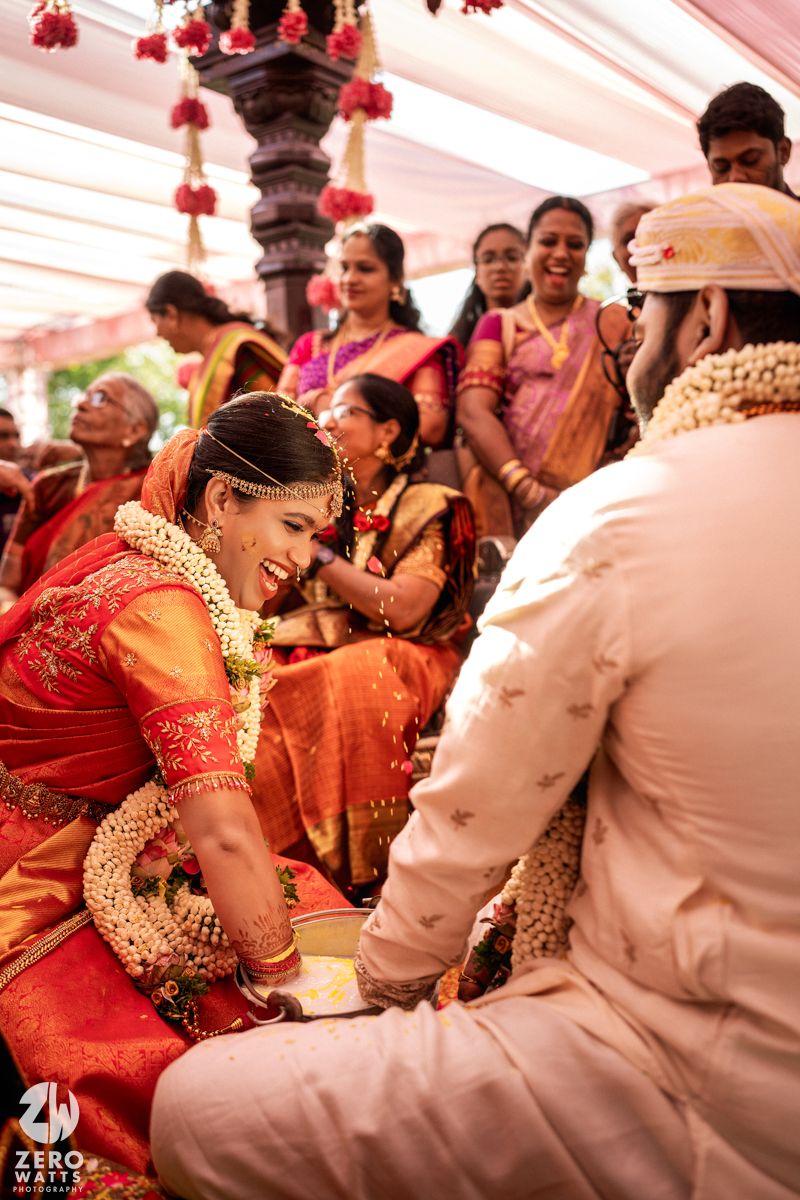 Smiling South Indian bride in red saree exchanging vows with groom at traditional ceremony.