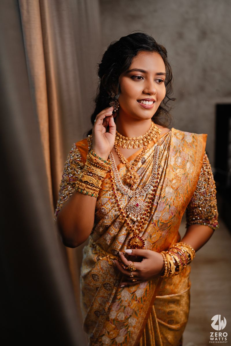 Traditional South Asian bridal portrait featuring ornate gold jewelry and orange silk attire.