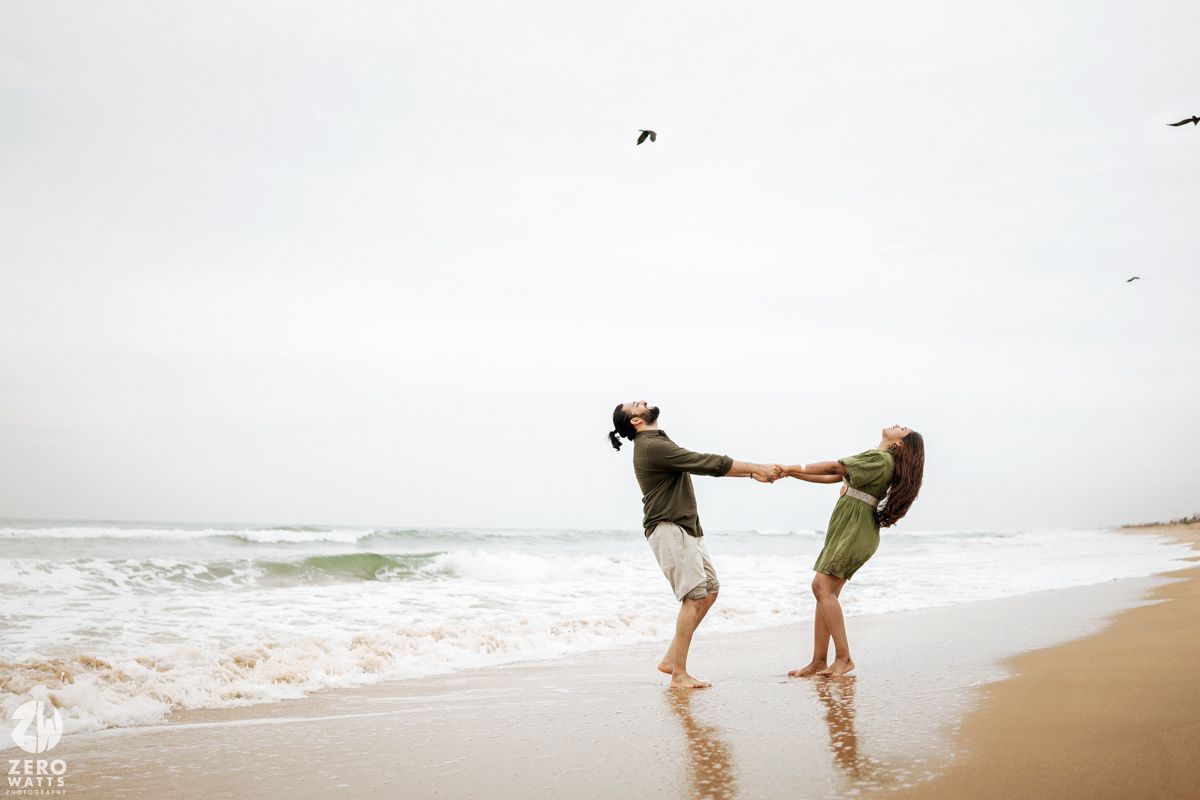 A couple shares a playful moment dancing on the beach near the ocean waves.