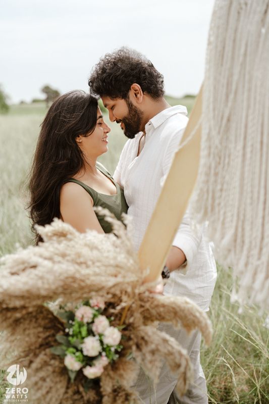 Romantic couple in white embraces in a dreamy outdoor setting with dried pampas grass and floral bouquet.