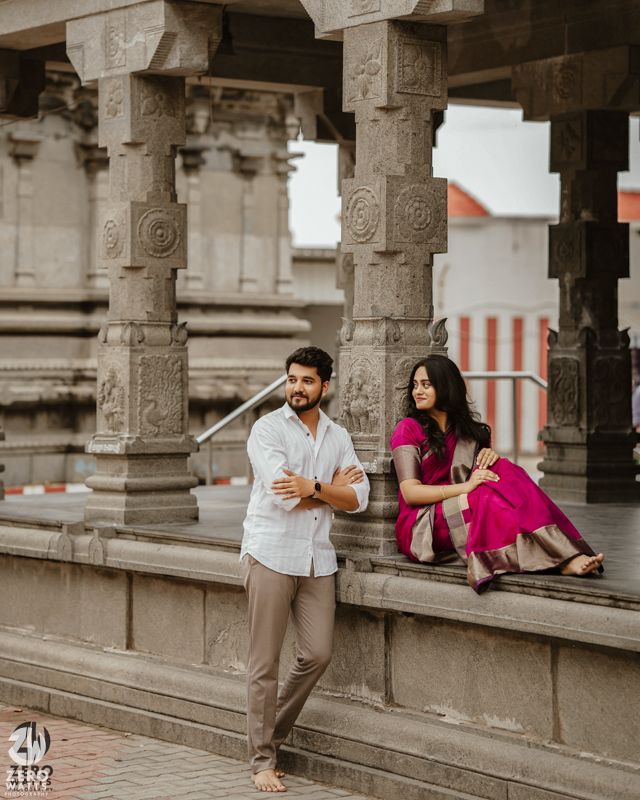 A couple poses against ornate stone pillars and archways of a traditional Indian temple architecture.