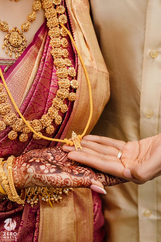 Close-up of ornate gold jewelry and henna decorated hands during a traditional Indian wedding ceremony.