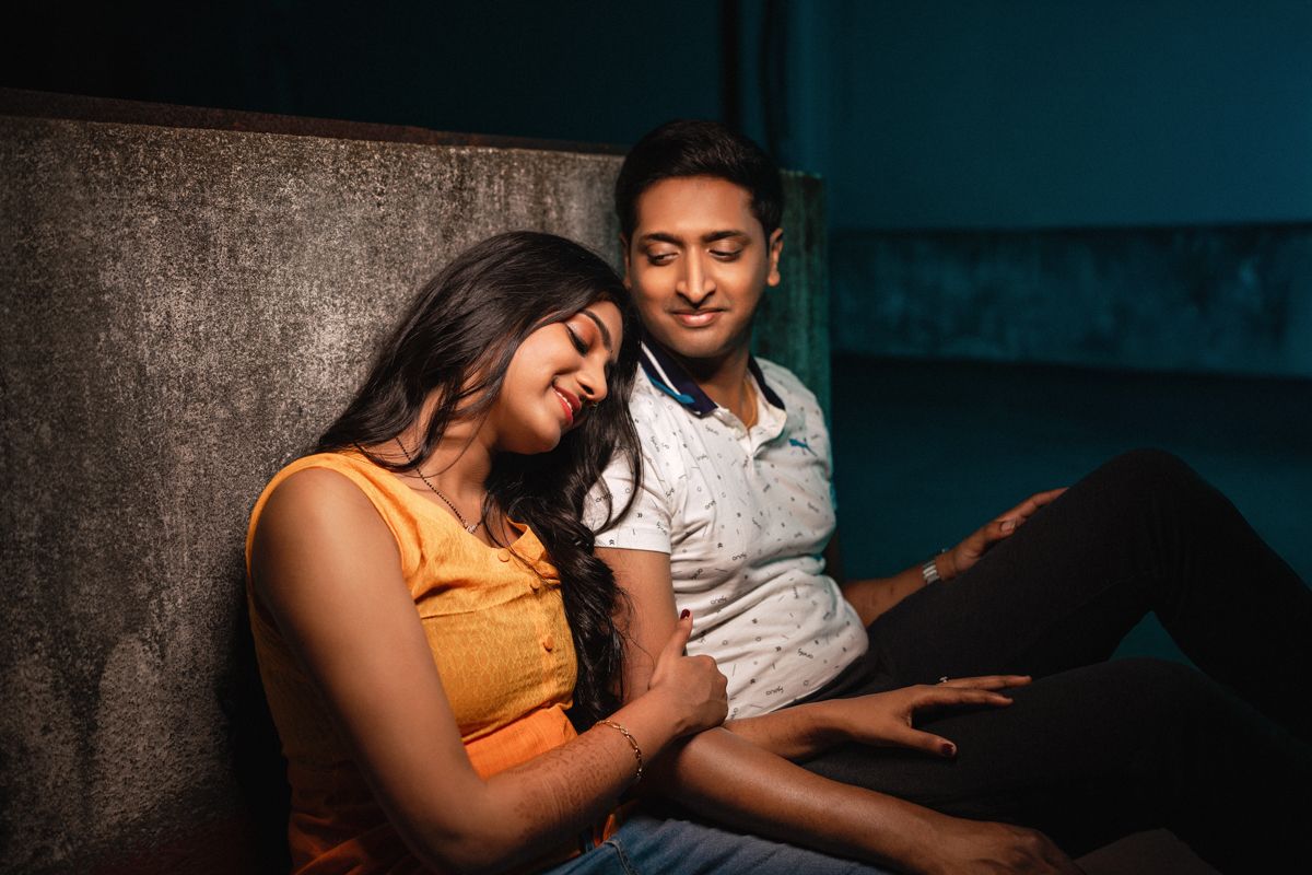 Couple relaxing on a couch in a dimly lit room with teal backdrop.