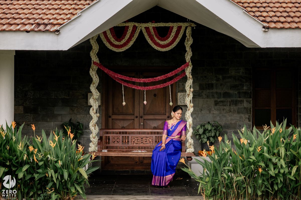 Traditional wooden porch swing decorated with garlands and red drapes at entrance of Kerala style home with garden.