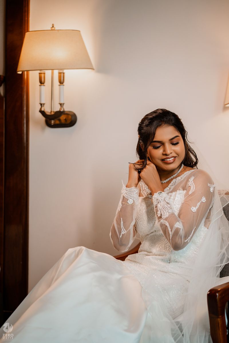 A bride in an elegant white wedding dress with long sleeves poses gracefully in a warmly lit room.