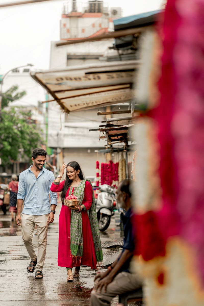 Couple walking together through colorful outdoor market with red decorations in the background.