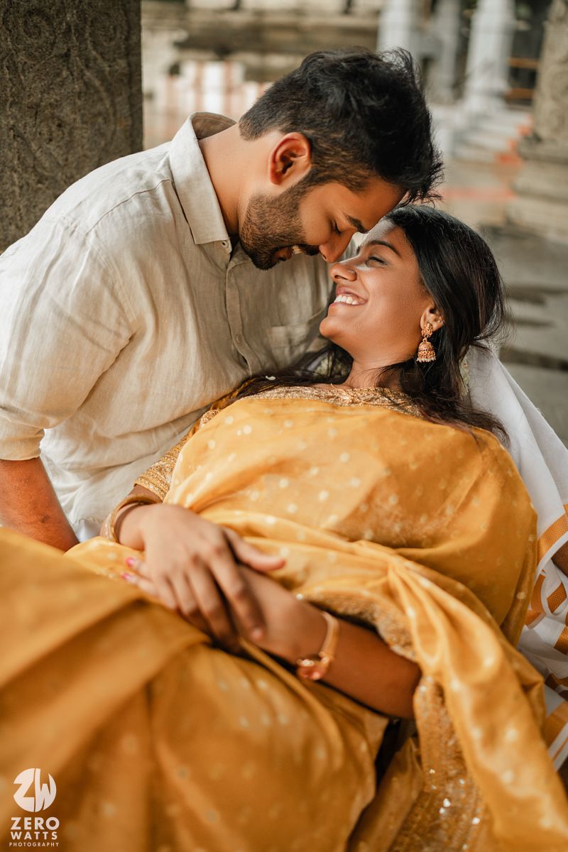 Romantic couple embracing while wearing white and gold attire against a stone backdrop.