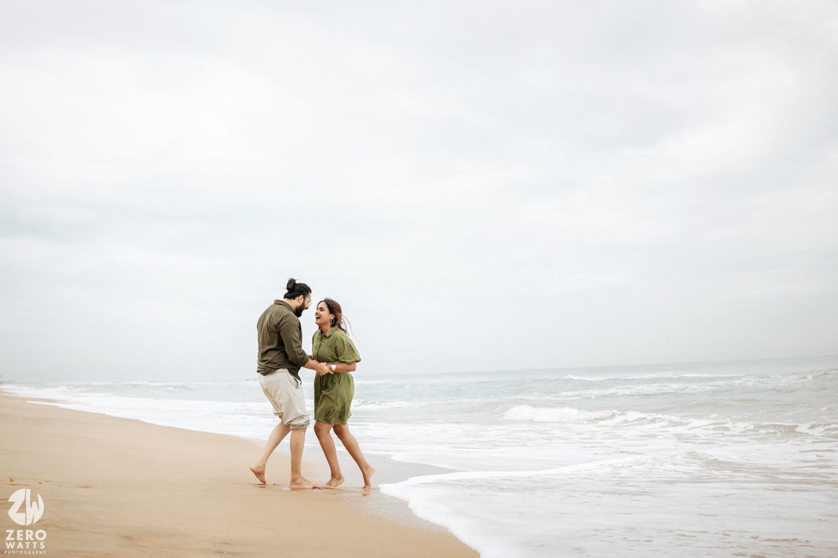Two people walking together along a misty beach shoreline with waves crashing in the background.
