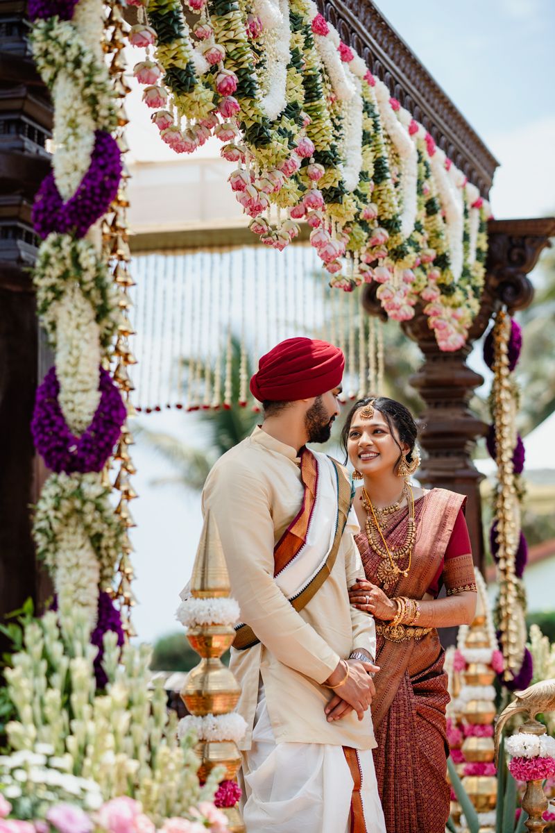 Outdoor wedding ceremony under decorated mandap with hanging floral arrangements and white draping.