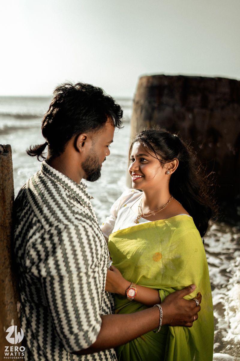 A romantic couple embraces on a beach at sunset, with one wearing a striped shirt and the other in yellow.