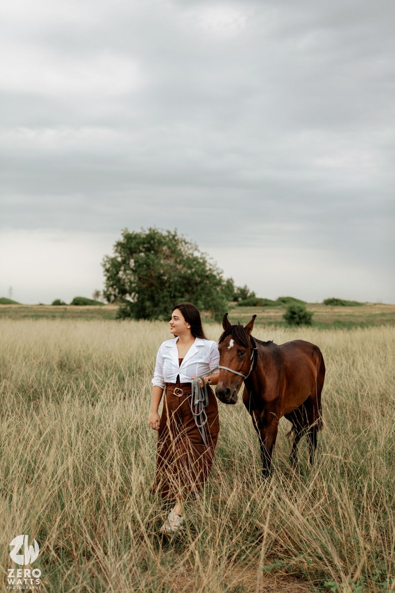 A brown horse stands beside its owner in a serene grassland setting under overcast skies.