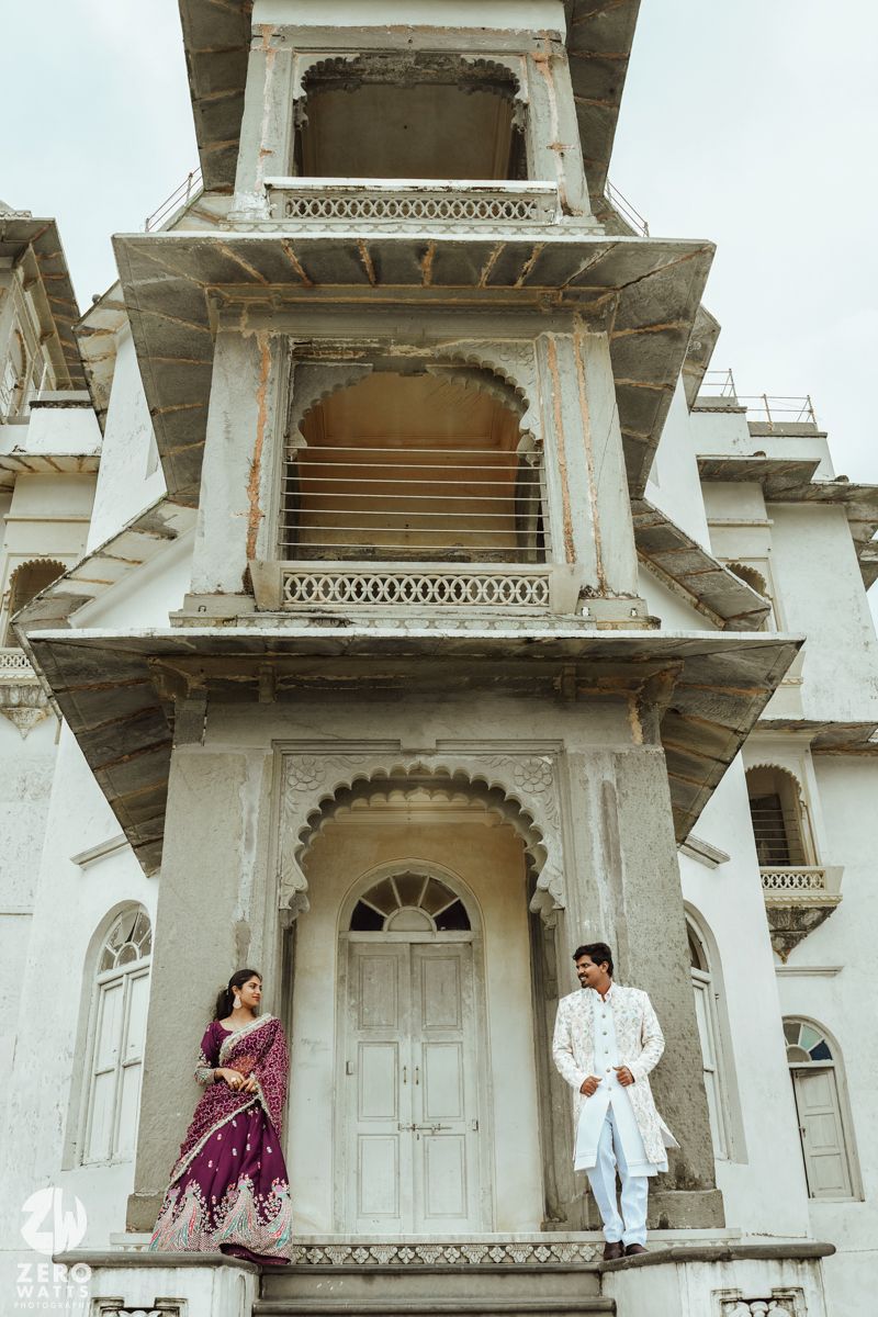 Romantic couple portrait against historic Indian palace architecture with white pillars and balconies.