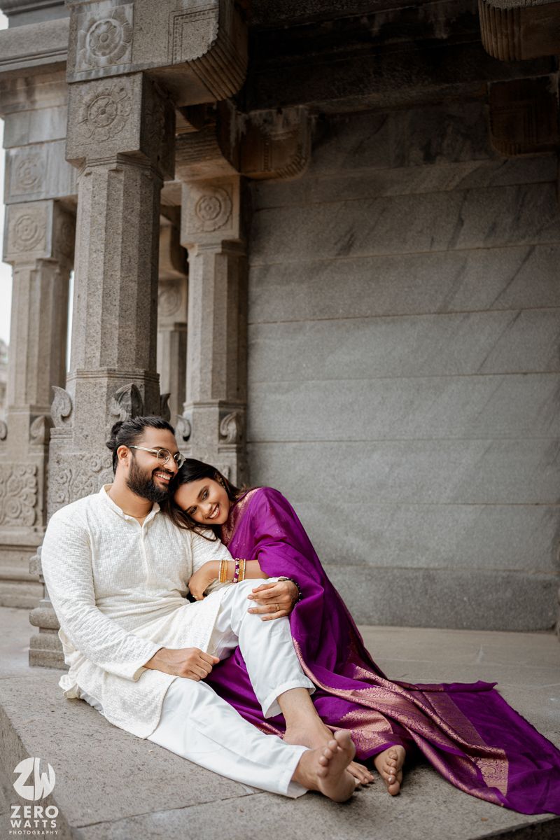Couple in white and purple traditional outfits share a joyful moment at a temple.