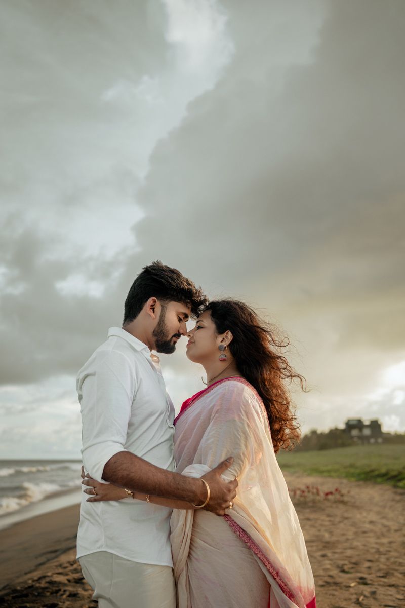 Intimate beachside moment captured against cloudy skies and ocean waves.