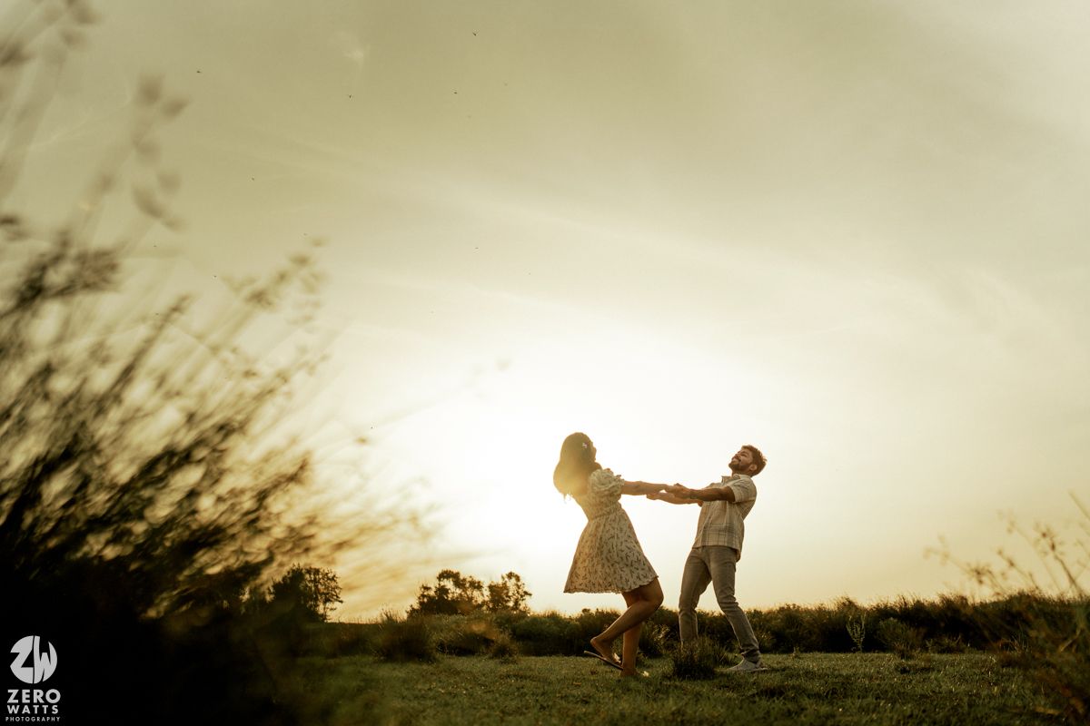 A silhouetted couple embracing on a hill against a golden sunset sky with tall grass swaying in the breeze.