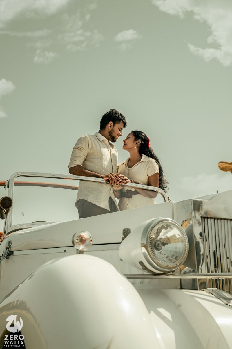 Elegant couple sharing a romantic moment in a classic white car against a muted green sky.