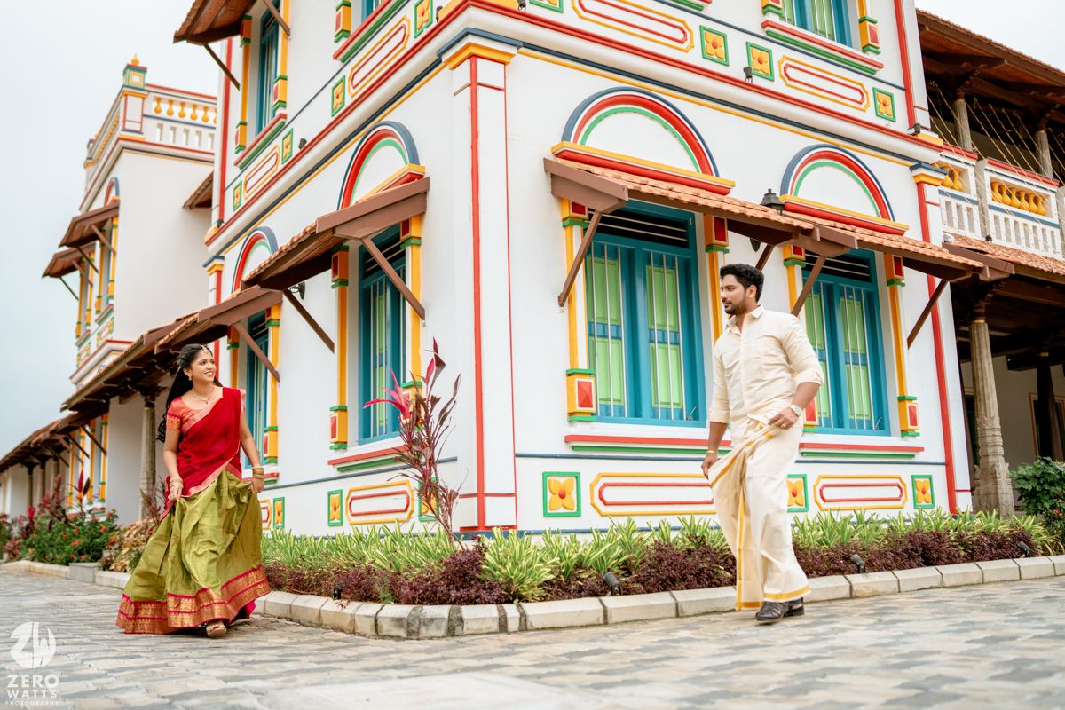Couple in traditional Indian attire posing outside a colorful heritage building with ornate architecture.
