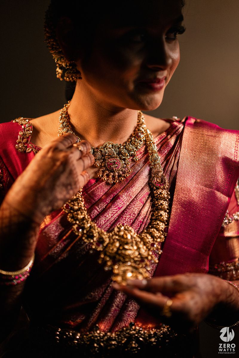 South Indian bride in pink silk saree adorned with traditional gold temple jewelry and mehndi hands.