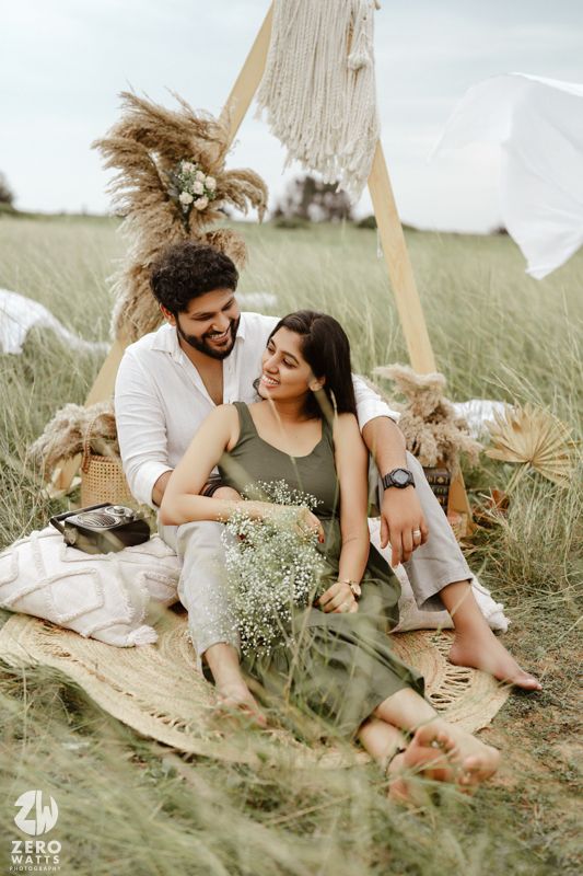 A couple shares intimate moments while lounging on blankets in a grassy meadow during an outdoor photoshoot.