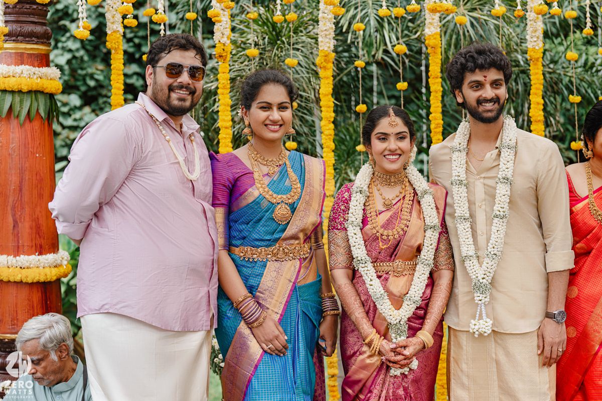 Traditional South Indian wedding gathering with guests in colorful attire under yellow floral decorations.