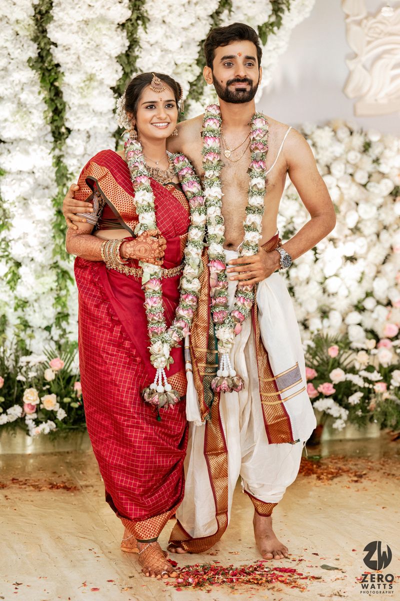 Traditional South Indian wedding ceremony with floral decorations and white backdrop.