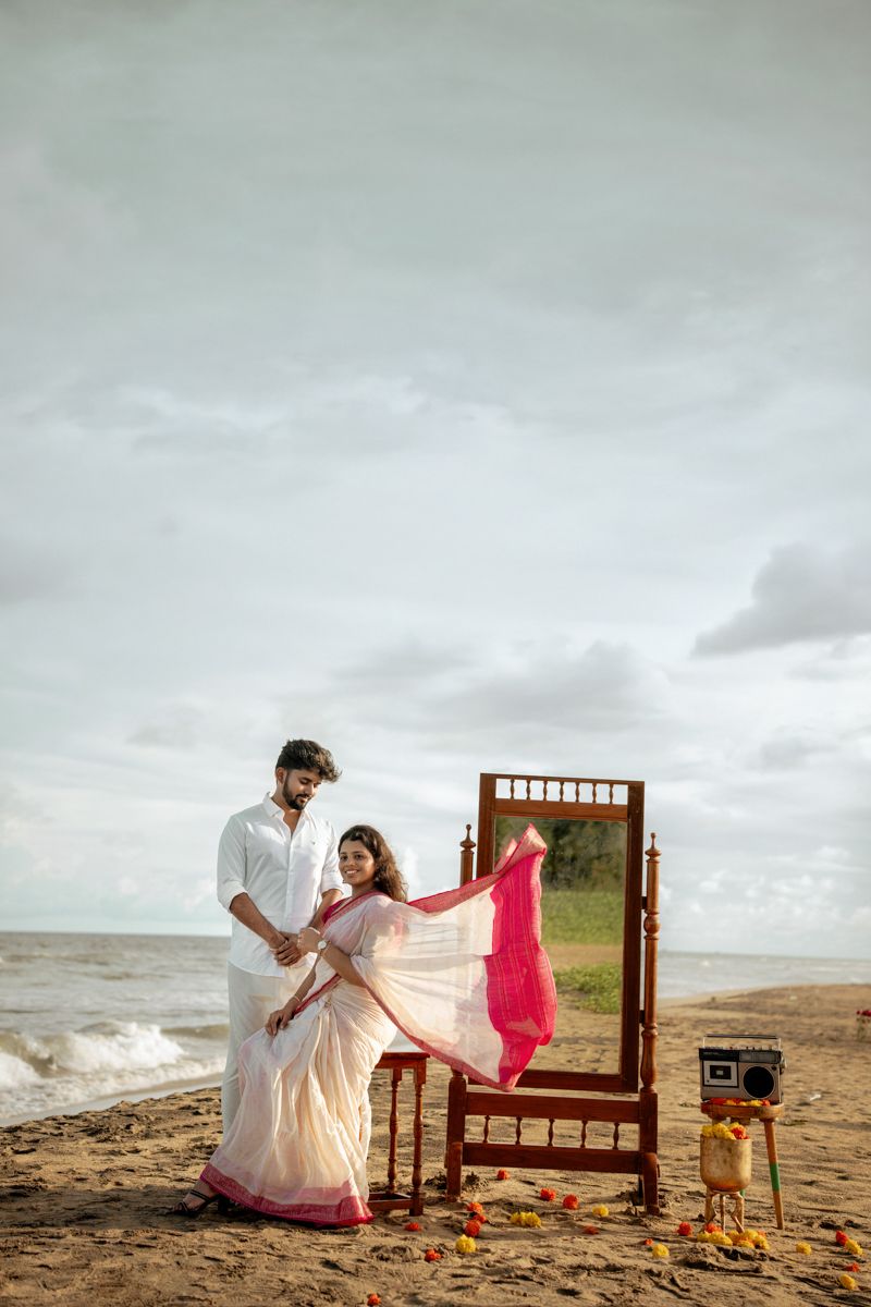 A dreamy beach scene with flowing fabric, wooden mirror frame and vintage props against a moody sky.