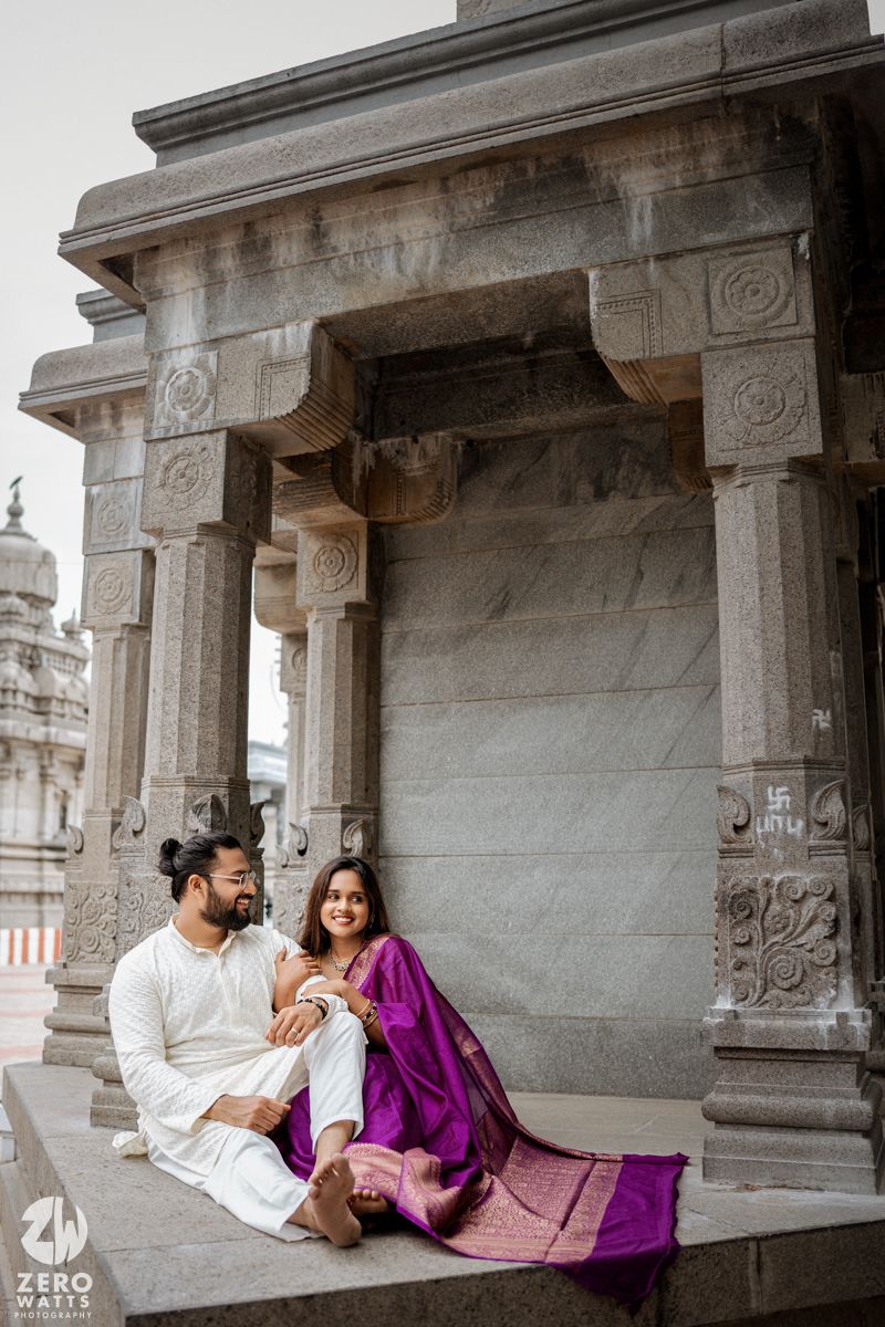 Couple in traditional Indian dress sitting together at a historic temple with ornate stone pillars.