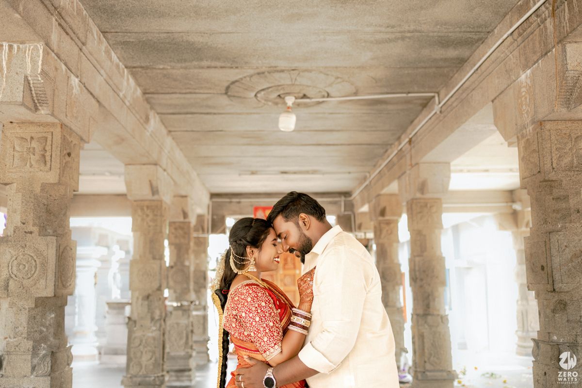 A couple embraces in a romantic moment under the ornate stone pillars of a historic architectural corridor.