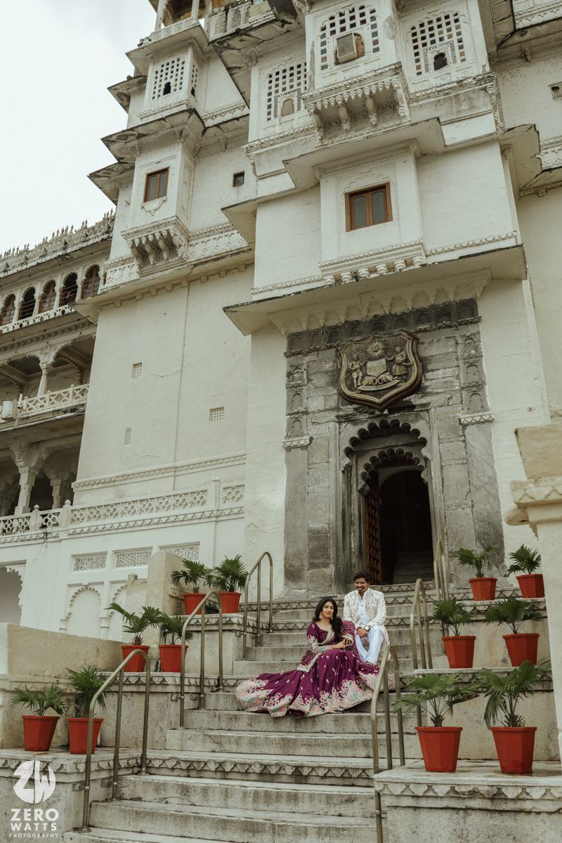 Traditional palace entrance with white walls and red potted plants framing stone steps and arched doorway.