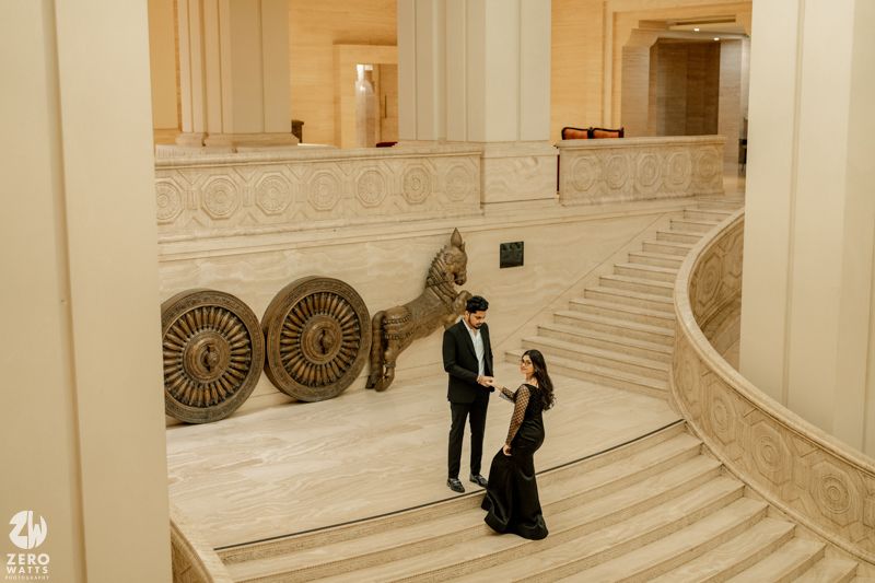 People sitting and walking on grand marble steps inside an ornate neoclassical building with decorative architectural details.