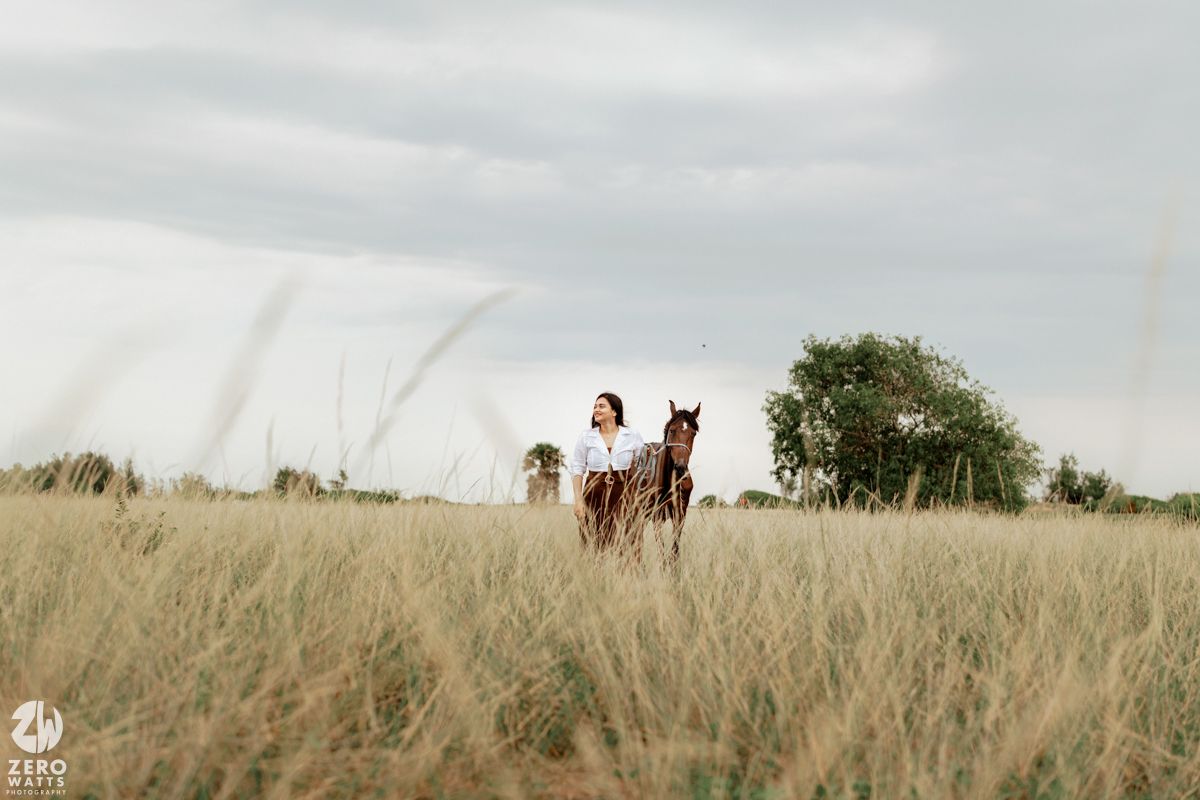 A panoramic view of horses grazing in a vast grassy field under cloudy skies.