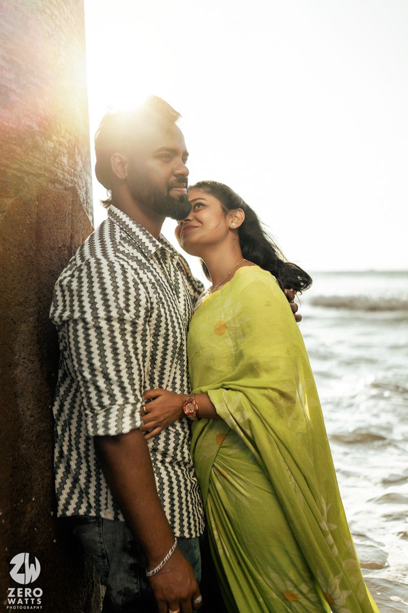 A couple shares an intimate moment by the ocean, wearing contrasting striped and yellow outfits.