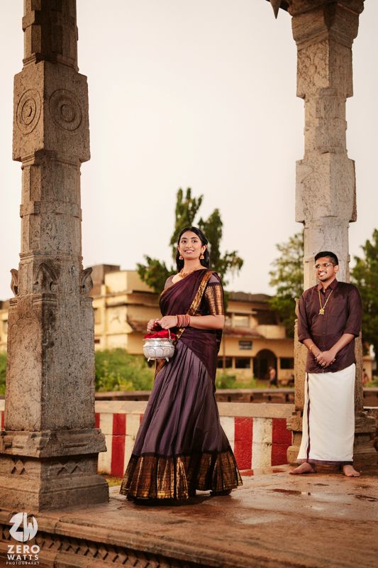 Traditional South Indian couple poses at ancient temple pillars during golden hour in elegant ethnic attire.