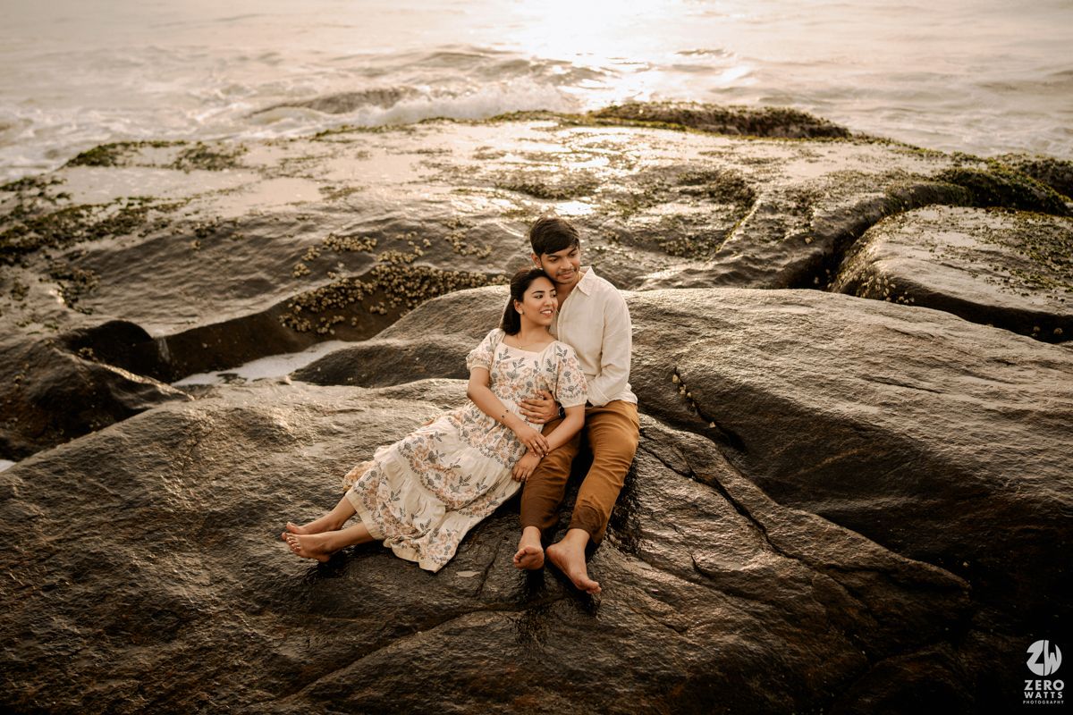 Couple lying on rocky coastal formation at sunset in romantic seaside photoshoot.
