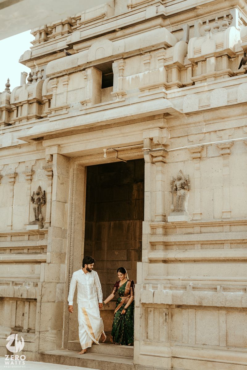 Indian couple in traditional attire holding hands at ornate Hindu temple entrance.