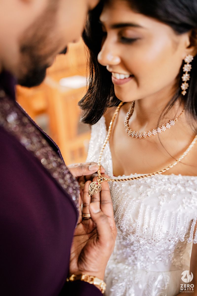 Close-up of Indian couple sharing a romantic moment as groom clasps a gold necklace on bride.