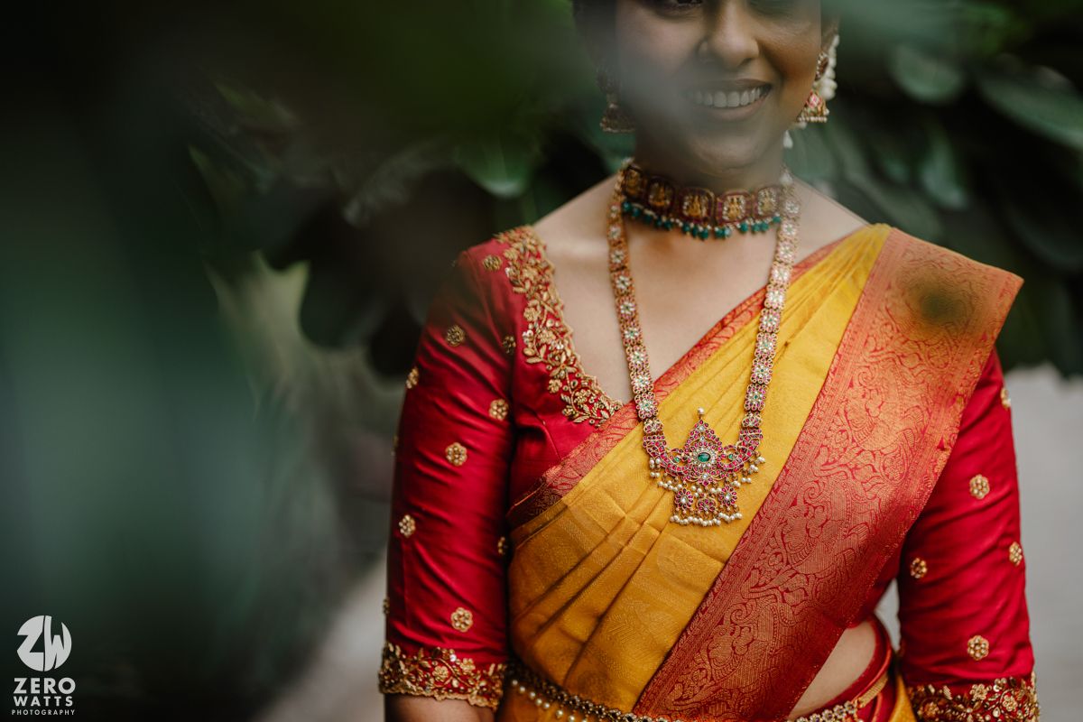 Traditional South Indian bride wearing yellow silk saree with red blouse and ornate gold temple jewelry.