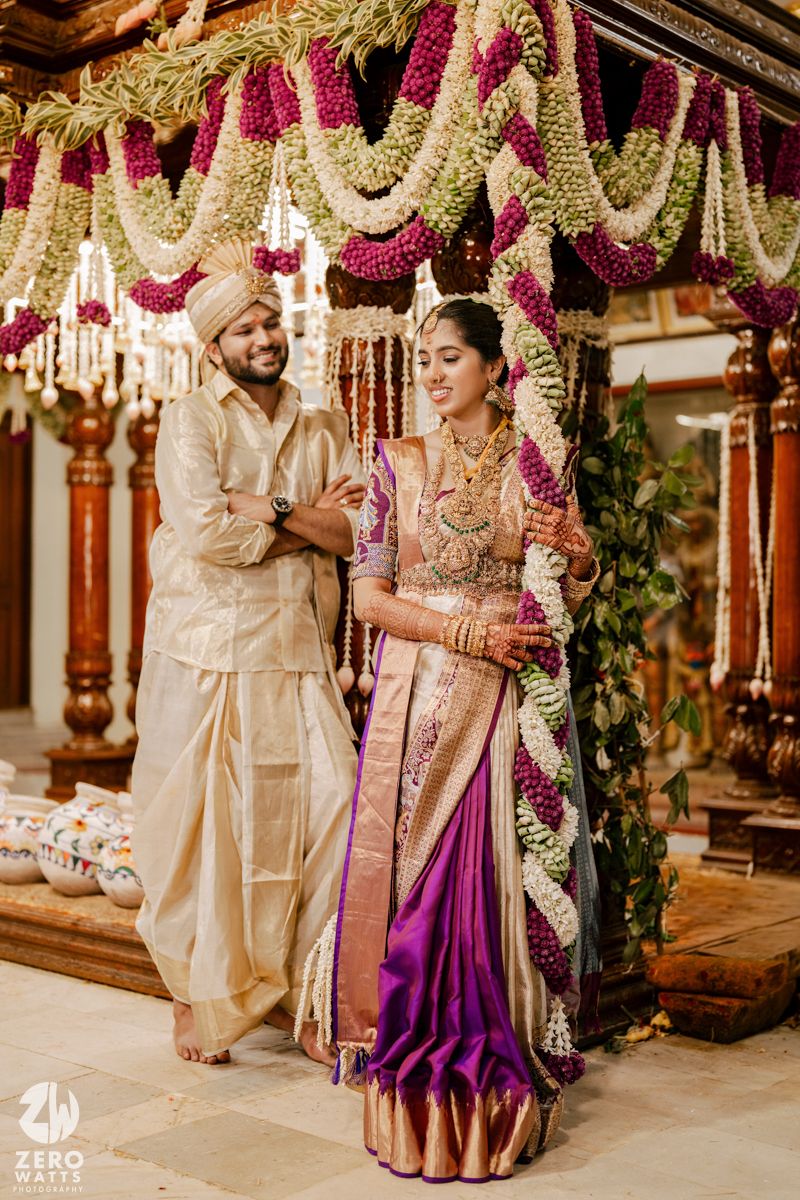 Wedding couple in traditional attire standing beneath ornate floral mandap decorations.
