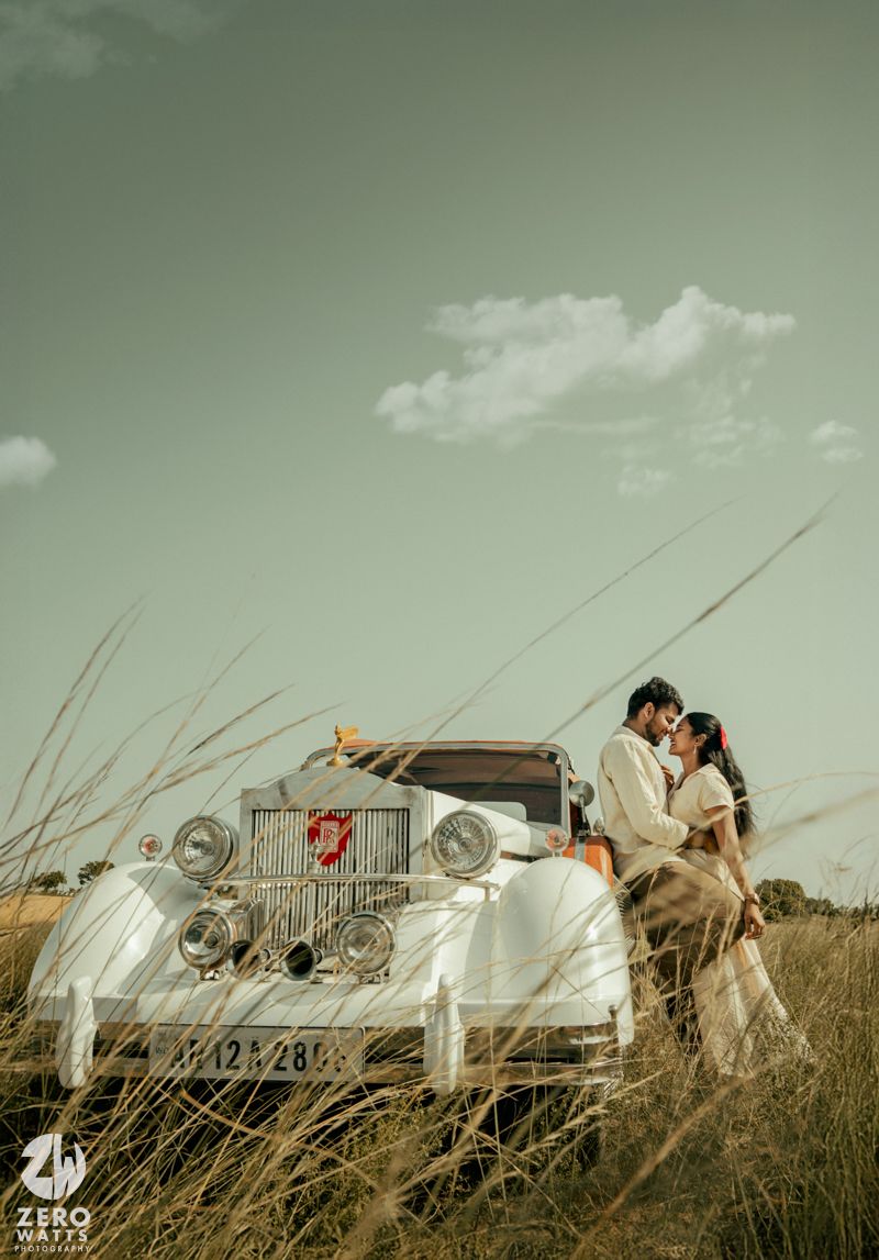 A vintage white Rolls Royce parked in tall grass against a cloudy sky creates a romantic backdrop.