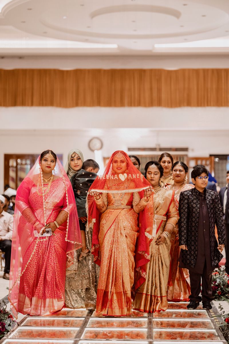 A group wearing colorful Indian wedding attire poses together in a bright indoor venue.