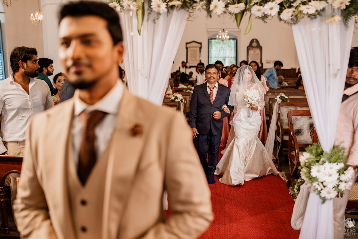 A wedding ceremony processional in a beautifully decorated church with white floral arrangements.