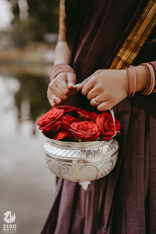 A person in dark clothing arranges vibrant red roses in a decorative silver bowl.